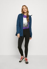 Veste légère bleue avec capuche, leggings noirs, t-shirt graphique violet et blanc, et baskets multicolores. Textures lisses, design décontracté.