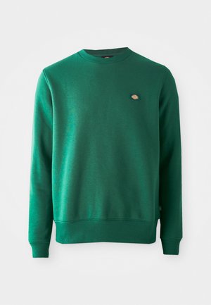 Grønn sweatshirt i bomullsblandet stoff. Har ribbestrikket rund halslinning, lange ermer og en liten logo-patch på brystet.