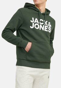 Green hoodie with white "JACK & JONES" logo, kangaroo pocket, drawstring hood, and ribbed cuffs and hem, paired with light grey sweatpants.