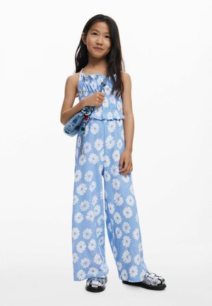 Salopetă albastră cu imprimeu floral, cu bust strâmtorat, picioare largi și volane stratificate. Asortată cu o geantă mică din denim și sandale argintii.