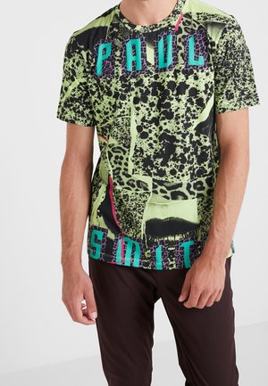Homme portant un t-shirt coloré à manches courtes avec un imprimé animal abstrait et le texte « PAUL SMITH » en lettres turquoise et violettes.