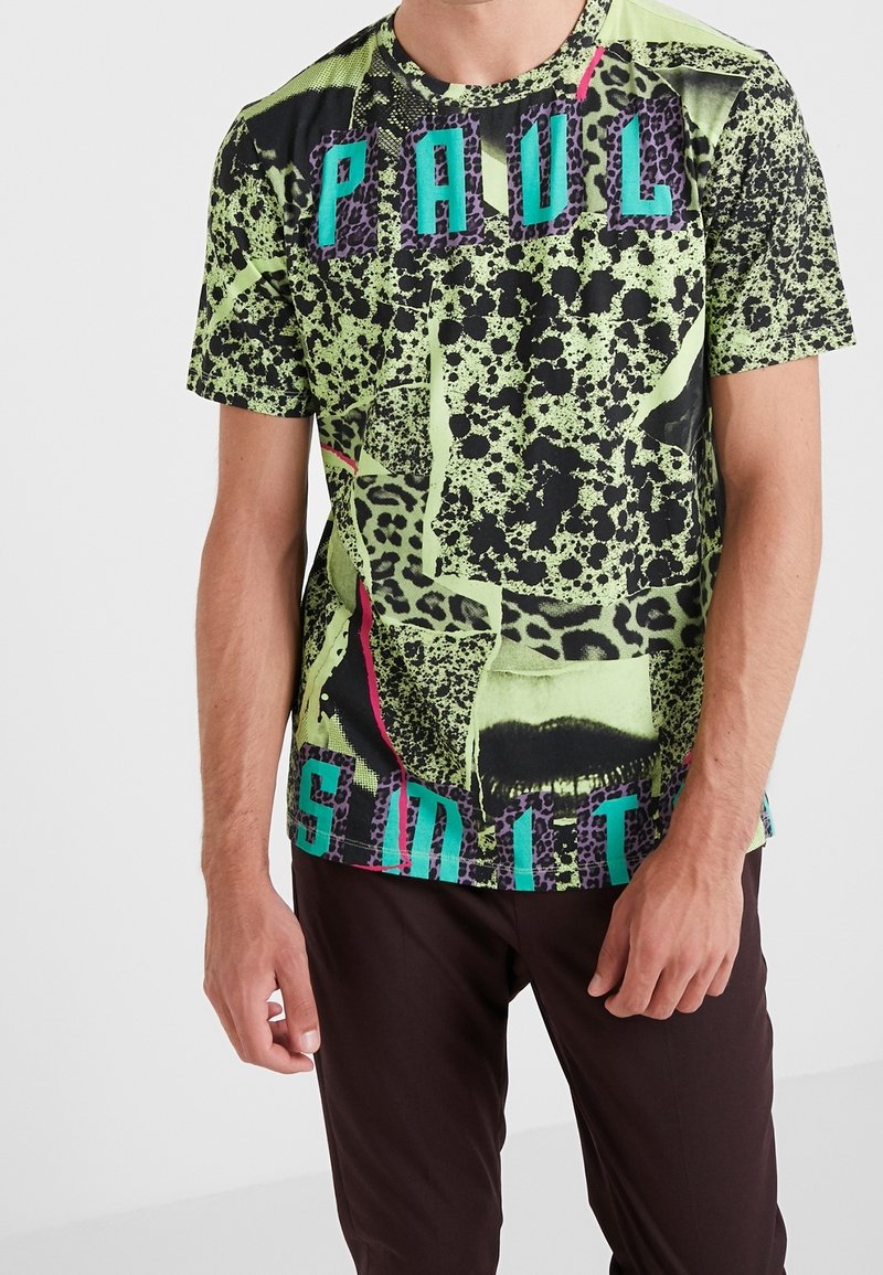 Homme portant un t-shirt coloré à manches courtes avec un imprimé animal abstrait et le texte « PAUL SMITH » en lettres turquoise et violettes.