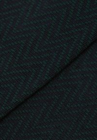 Ciemna dzianina z wzorem w rybie łuski w odcieniach zieleni i granatu. Tekstura wydaje się miękka i przytulna, o średniej grubości.