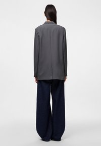Szürke, oversize blézer, hátul egyetlen szellőzőnyílással, széles lábú sötétkék farmernadrággal párosítva. Egyszerű, letisztult dizájn.