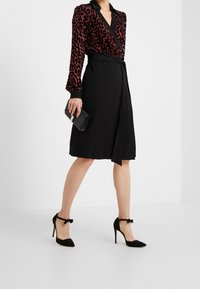 Sort omslagskjole med en leopardmønstret velourtop, lange ærmer og en båndliv. Sammen med sorte spidse hæle og en clutch.