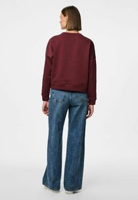 Burgunderfarget kort sweatshirts med rund hals, laget i flanellmateriale, og med senkede skuldre, kombinert med høyt liv og vide blå jeans.