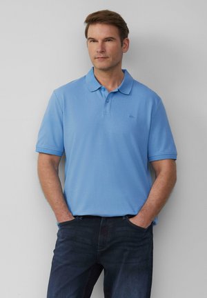 Polo shirt bleu clair avec col, manches courtes et texture subtile ; associé à un jean foncé. Présente un logo sur la poitrine.
