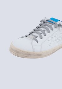 Weiße Leder-Sneaker mit grauen Schnürsenkeln und einer strukturierten Oberfläche, die an der Seite perforierte Details aufweist und eine leicht abgenutzte beige Sohle hat.