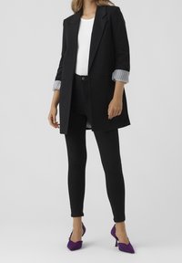 Musta pitkä bleiseri valkoisen paidan päällä, yhdistettynä mustiin kireisiin farkkuihin ja purppuranvärisiin teksturoituihin korkokenkiin. Raidalliset hihansuut näkyvissä.