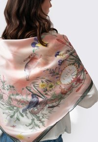 Foulard en soie avec un fond rose pastel ornée d'illustrations florales et animales, comprenant un lapin et un oiseau bleu, ainsi qu'une bordure décorative.