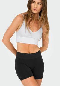 Λευκό ριχτό μπλουζάκι με V-λαιμό και μαύρες σορτς με φαρδύ ελαστικό ζωνάκι, και τα δύο φτιαγμένα από ελαστικό υλικό για άνεση και κίνηση.