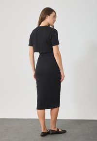 Μαύρο ριμπ μίντι φόρεμα με εφαρμοστή σιλουέτα, διαθέτοντας κοντά μανίκια και σχισμή στην πλάτη. Λεπτή υφή και μήκος μέχρι το γόνατο.