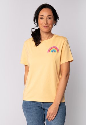 T-shirt en coton jaune à manches courtes, avec un graphisme arc-en-ciel multicolore et le texte "POUVOIR DES FEMMES" en dessous.