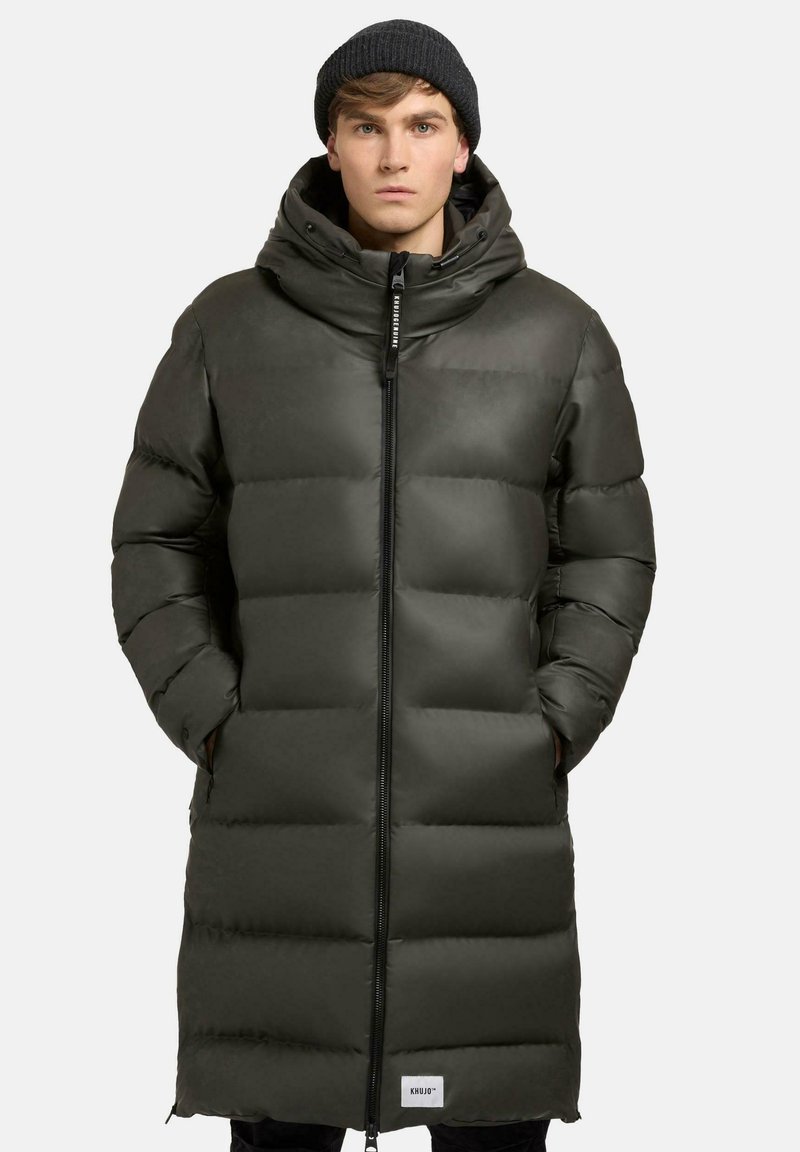 Lang, polstret parka i mørkegrøn med høj krave, lynlås foran og sidelommer. Har en glat tekstur og synligt quiltet mønster.