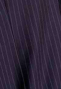 Laivastonsininen kangas, jossa pystysuorat valkoiset ohutraidat, teksturoitu pinta ja pehmeä laskeutuvuus, esittelee hienostunutta materiaalia ja jäsenneltyä kuviota.