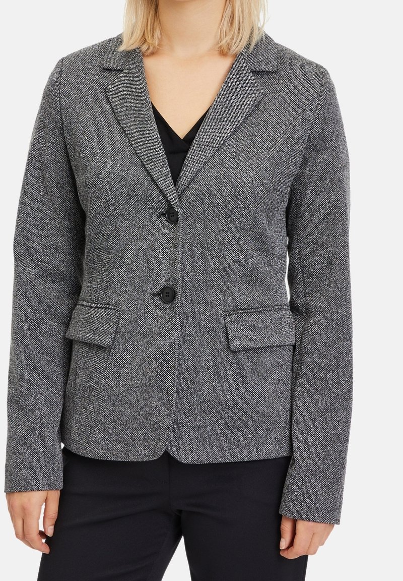 Grå tweedblazer med slagkrage, två framfickor och dubbelknäppning. Texturerad tyg med ett subtilt mönster.