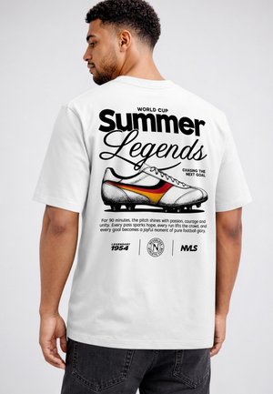 Man wearing white T-shirt with black text and vintage soccer cleat graphic, referencing World Cup and football passion on the back.