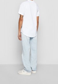 Biała koszulka z krótkim rękawem w połączeniu z jasnoniebieskimi podartymi dżinsami i białymi trampkami. Koszulka ma zaokrąglony dół, a dżinsy mają przetarcia.