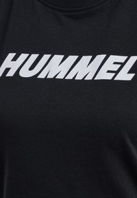 Zwarte stof met grote, vette witte tekst met de tekst "HUMMEL" over het borstgebied van een kledingstuk.