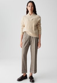 Beige gebreide sweater met een sjawlboord, gecombineerd met bruin geruite broeken met omslag. Model draagt bruine instappers.