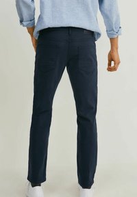 Námořnické modré kalhoty z měkké tkaniny, slim-fit design se zadními kapsami, spárované se světle modrou košilí a bílými teniskami.