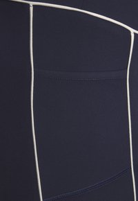 Jūras spēku aktīvā apģērba legingi tumši zilā krāsā ar baltu akcentu šuvēm, ar sānu kabatu un gludu, struktūru audumu komfortam un elastībai.