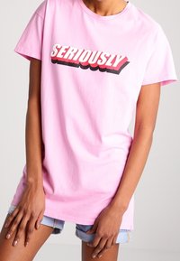 Růžové bavlněné tričko s krátkými rukávy a kulatým výstřihem. Na přední straně se vyjímá výrazný nápis "SERIOUSLY" v červené a černé barvě.