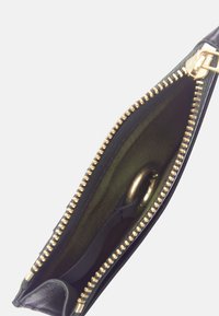 Pochette en cuir noir avec fermeture éclair dorée partiellement ouverte, révélant un intérieur en tissu vert et deux bagues dorées à l'intérieur.