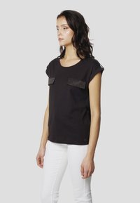 Must lühikeste varrukatega T-särk kahe tekstuurilise taskuga. Valmistatud pehmest kangast, ümar kaelus ja lõdva istuvusega.