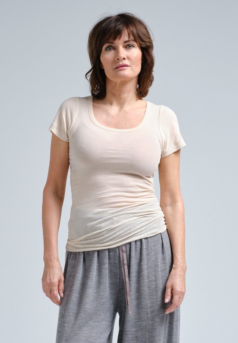 T-shirt ajusté beige clair à manches courtes et décolleté en cœur, associé à un pantalon gris ample avec taille à cordon.