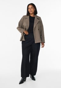 Braun karierter Blazer mit Reverskragen, schwarzes Oberteil, hochtaillierte dunkle Jeans mit weitem Bein und schwarze spitze Stiefeletten.