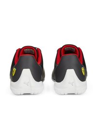 Čierne syntetické tenisky s červenými akcentmi, s perforovaným dizajnom, bielymi podrážkami a žltým logom Ferrari na zadnej strane.