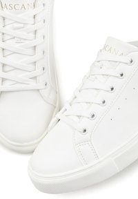 White sneakers made of synthetic leather, featuring flat laces, perforations on the sides, and a textured rubber sole. Gold logo on tongue.