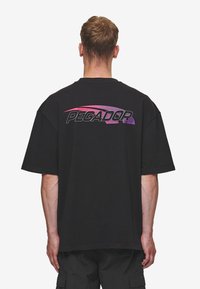 Černé oversized tričko s velkým logem "PEGADOR" ve fialovém gradientu na zadní straně; krátké rukávy, kulatý výstřih, bavlněný materiál.