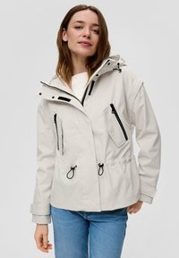 Hellgraue Jacke mit Kapuze, ausgestattet mit schwarzen Reißverschlüssen und Kordelzügen, zwei Fronttaschen und verstellbaren Bündchen. Wasserdichtes Material.