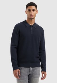 Marineblauwe polo met lange mouwen, voorzien van een textuurpatroon op de borst en effen mouwen, met een kraag en knoopsluiting.