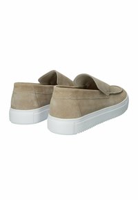 Béžové semišové slip-on topánky s bielou gumovou podrážkou a zaobleným dizajnom, ktorý obsahuje plochý, široký popruh cez hornú časť.