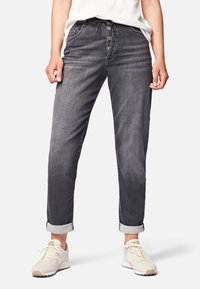 Jeans de mezclilla gris con corte relajado, diseño de cinco bolsillos, cierre de botón y puños enrollados. Llevados con zapatillas de color claro.