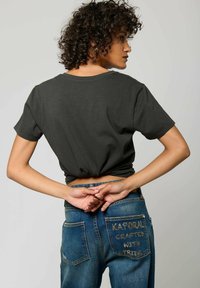 T-shirt à manches courtes gris foncé avec un ourlet noué, associé à un jean en denim bleu avec un texte brodé sur la poche arrière.