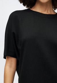 Black cotton-blend oversized t-shirt with a rounded neckline and short sleeves, featuring a smooth texture and subtle stitching details.