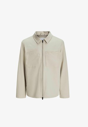 Beige jasje van zachte stof, met een kraag, een voorrits en twee grote borstzakken. Lange mouwen met een relaxte pasvorm.