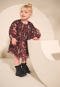 Drukāta puscaurspīdīga kleita ar ziedu rakstiem bordo krāsā, ar pufotām piedurknēm. Melni spīdīgi potīšu zābaki ar mežģīnēm un apaļu purngalu.