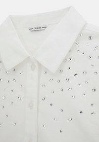 Weißes Hemd mit Kragen und Knöpfen sowie verstreuten silbernen Strasssteinen, mit der Marke GUESS im Kragen.