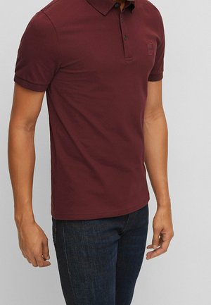 Polo bordeaux avec col classique, manches courtes, patte de boutonnage à trois boutons et petit logo sur la poitrine. Matière en coton texturé.