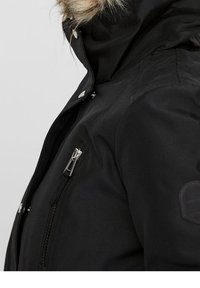 Veste d'hiver noire avec capuche bordée de fausse fourrure, poche poitrine zippée, fermetures à pression, et un tissu lisse et texturé.