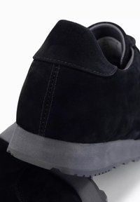 Musta mokkanahka lenkkarit, joissa on teksturoidun pinnan, harmaa kumipohja ja näkyvät saumat kantapään kohdalla. Minimalistinen muotoilu, jossa on klassinen siluetti.