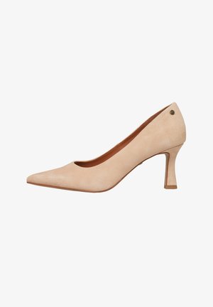 Beige suède pump met een spits toelopende neus, een slanke hak van gemiddelde hoogte en een klein rond metalen logo nabij de hielrand.