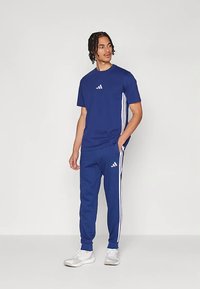 Μπλε αθλητική φόρμα που αποτελείται από ένα t-shirt με μικρό λογότυπο και παντελόνια με τρεις λευκές πλαϊνές ρίγες και ταιριαστά λογότυπα.