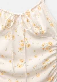Top floral cu fundal crem, cu flori galbene, textură adunată, curea ajustabilă la gât și dantelă pe margini.