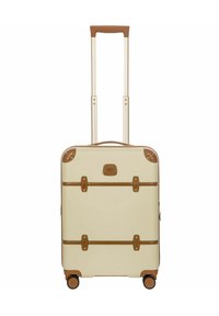 Maleta crema con detalles marrones, asa retráctil, cuatro ruedas y correas similares a un cinturón; textura suave con forma angular.